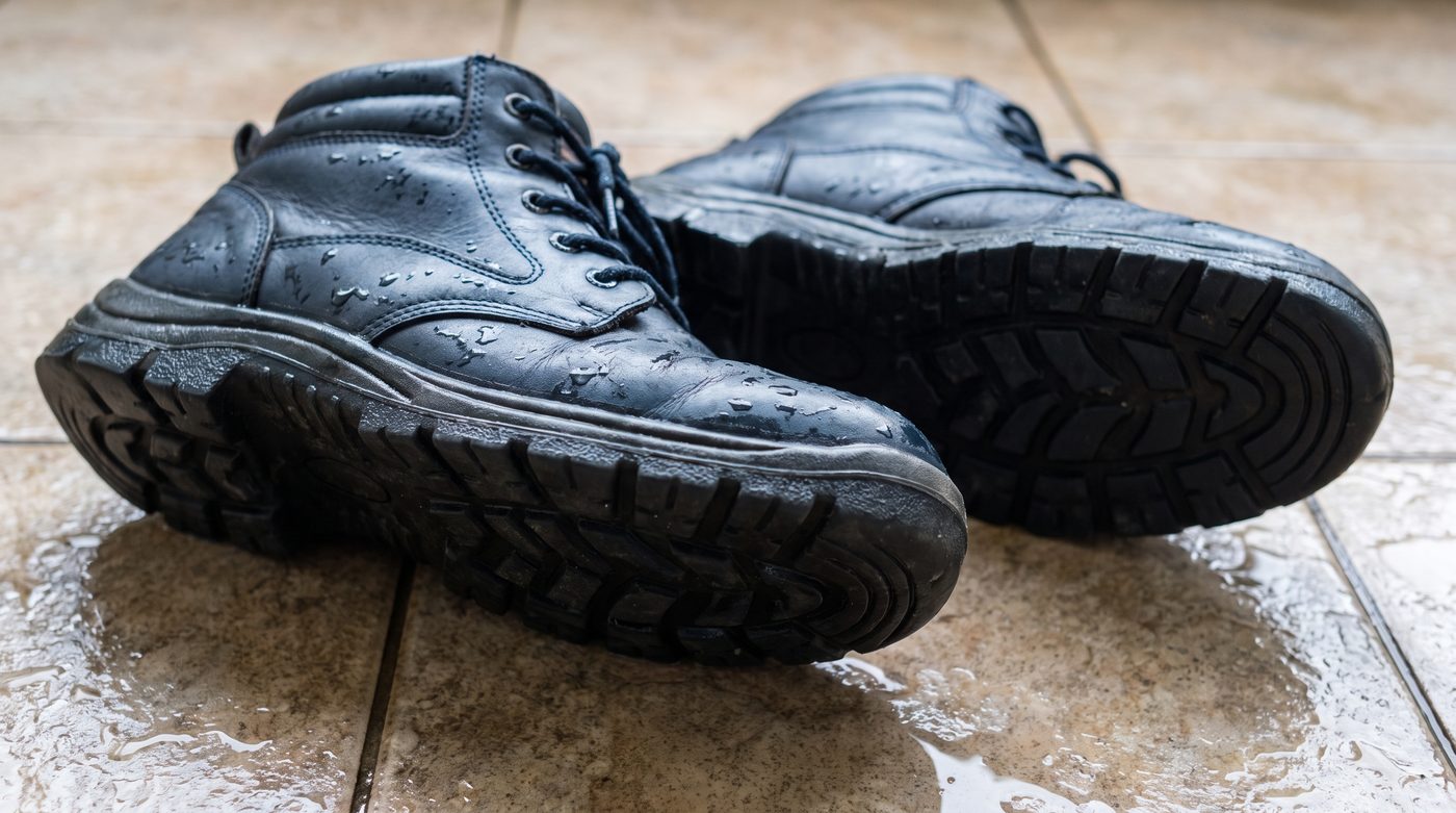 A pair of branded safety boots on a wet tiled floor showing the tread pattern on the sole